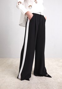 Svarta vida byxor med vita sidostrecken, fylld design och spetsiga fållar. Tyget är slätt; har sidofickor.