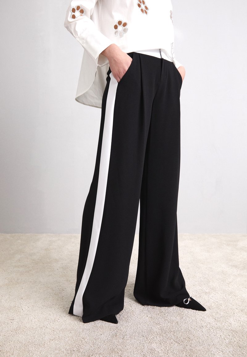 Svarta vida byxor med vita sidostrecken, fylld design och spetsiga fållar. Tyget är slätt; har sidofickor.