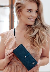 Navy blue textured wallet with a snap closure, featuring a silver logo accent. The design is rectangular and smooth with visible grain.