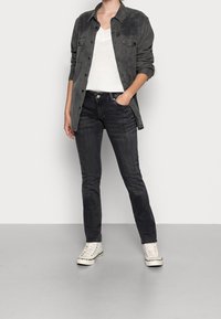 Mörkgrå jeans i slim fit, matchat med en vit stickad v-necktröja och en svart skjortjacka, avslutat med vita sneakers.