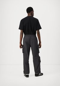 T-shirt de algodão preto combinado com calças cargo cinza-escuras com bolsos laterais, cintura elástica e fechos de correr, projetadas para utilidade e conforto.