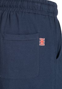 Tamne plave trenirke od mješavine pamuka, s elastičnim pojasom i stražnjim džepom na kojem se nalazi mali emblem Union Jacka.