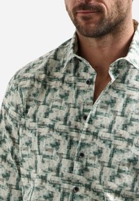 Een button-up shirt met een groen-wit abstract patroon, gemaakt van lichtgewicht stof met een spread collar en zwarte knopen.