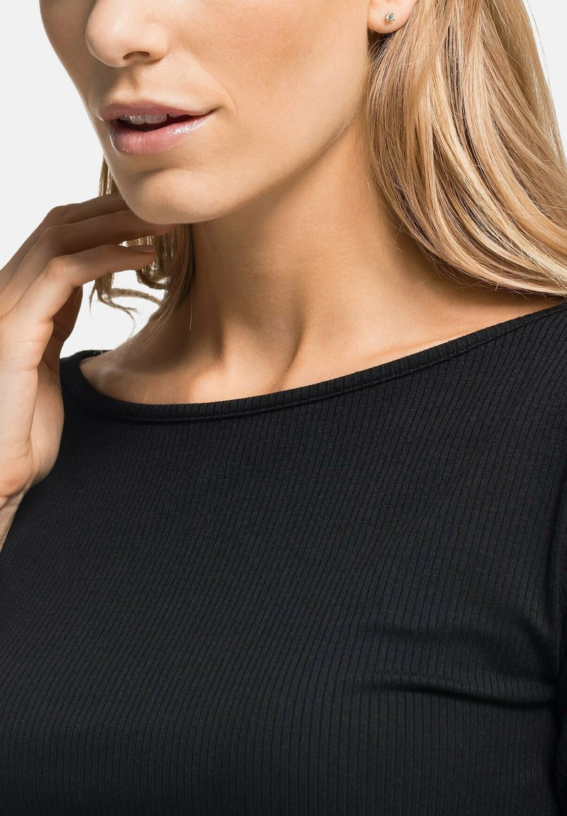 Schwarzes geripptes Oberteil mit schulterfreiem Ausschnitt. Glatte Stofftextur, figurschnittige Passform und dezenter Glanz auf den Lippen mit Steckerohrringen.