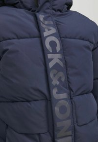 Navyblå puffjacka med en glansig logoband med texten "JACK&JONES", kviltad textur och en sidficka.