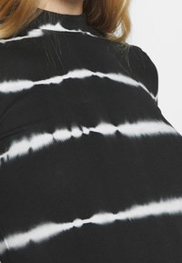 Czarna i biała koszulka z długim rękawem i wysokim kołnierzem w stylu tie-dye. Tkanina ma prążkowaną fakturę i poziome faliste wzory.