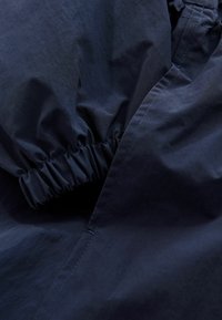 Tissu bleu foncé avec poignet élastique froncé et couture visible, probablement partie d'une manche ou d'une jambe de pantalon.