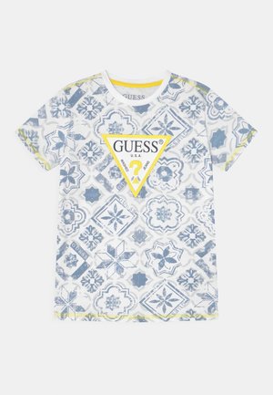 T-shirt blanc à manches courtes avec motifs floraux géométriques bleus et un logo GUESS triangle jaune au centre devant.