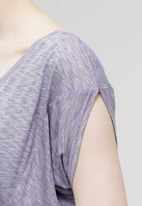 Top corto a maniche corte a righe viola con scollatura a V, caratterizzato da una vestibilità ampia e dettagli delle maniche ripiegati. Il tessuto ha un aspetto morbido e testurizzato.