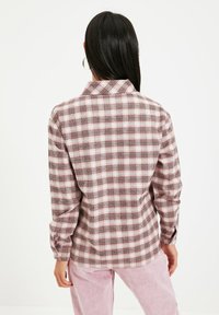Camicia di flanella a quadri in tonalità di rosa e rosso. Presenta un colletto, maniche lunghe e polsini con bottoni. Tessuto morbido con una vestibilità rilassata.
