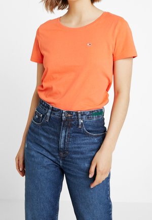 Orange cotton t-shirt with short sleeves and a round neckline, paired with dark blue high-waisted denim jeans featuring visible stitching.