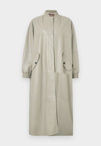 Dlhý béžový kožený kabát s rebrovaným golierom a manžetami, vreckami so zapínaním na cvoky vpredu a skrytým zapínaním na gombíky.