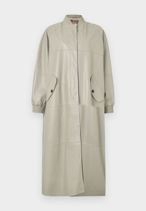 Pitkä beige nahkainen takki, jossa on resorikaulus ja resoriset hihansuut, etutaskut nappilistoilla ja piilotettu napitus.