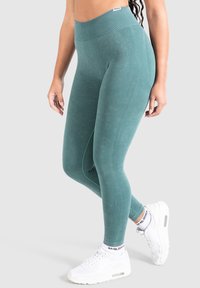 Leggings teal a vita alta in un morbido tessuto testurizzato, con dettagli a coste e sottili accenti di cucitura, abbinati a sneakers bianche.