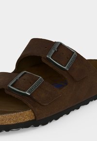 Sandale Birkenstock en daim marron avec deux boucles métalliques réglables et semelle en liège, présentée en gros plan sur fond blanc.