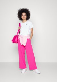 T-shirt Nike blanc, pantalon oversized rose,pull léger rose noué à la taille, et sac à main rose avec des accents en fausse fourrure. Baskets blanches.