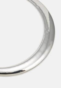 Gros plan d'un objet métallique incurvé en argent poli ou chrome sur fond blanc, montrant les détails de la surface réfléchissante.