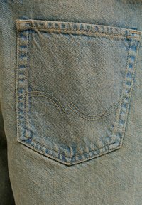 Kahvatasku kulunud sinistes teksapükstes, millel on topeltõmblusega kõver õmblusdetail ja nähtav õmblusääre ümber.