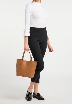 Braune, perforierte Tragetasche mit strukturierter Form und zwei Griffen, kombiniert mit schwarzen, schlanken Hosen und einem weißen, hohen Rundhalstop.