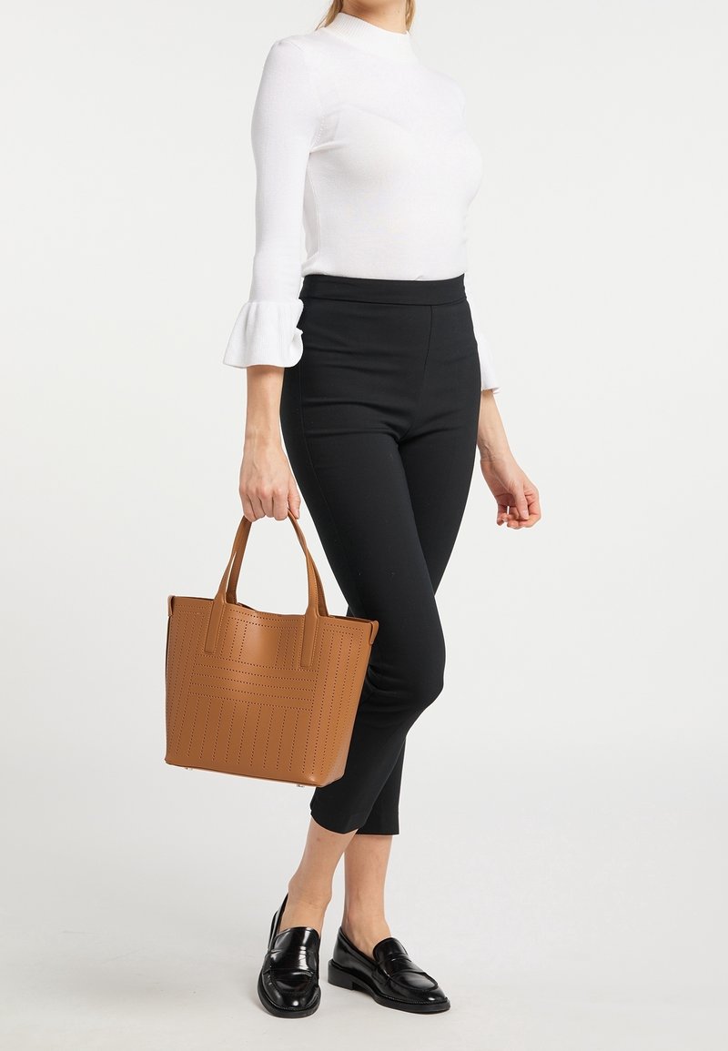 Sac fourre-tout marron perforé à forme structurée et double poignée, associé à un pantalon slim noir et un haut col montant blanc.