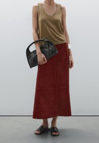 Olivengroene mouwloze top, rode suède maxi-rok, zwarte handtas met een gebogen handvat, en zwarte slidesandalen. Zilveren manchet om de pols.