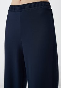 Marineblauwe sportbroek met een elastische tailleband, gladde stof en zijpanelen van mesh. Kenmerkt zich door een relaxte pasvorm en rechte snit.