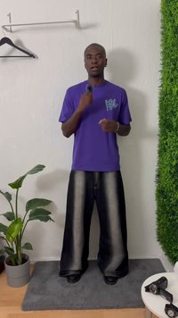 T-shirt roxa com um design gráfico, combinada com jeans de perna larga em preto e cinza. O visual é complementado por botas pretas.