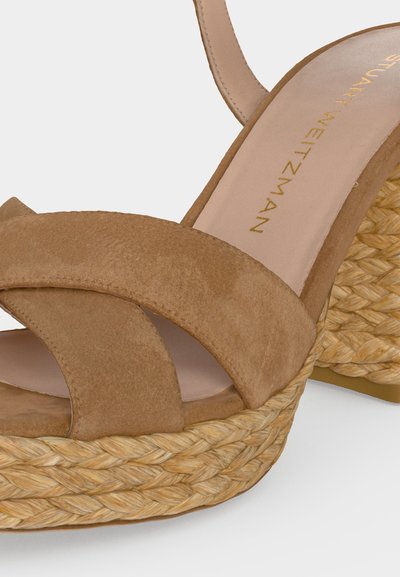Sandale compensée en daim beige avec plateforme en corde tressée et bride à la cheville, avec logo Stuart Weitzman doré estampé sur la semelle intérieure.