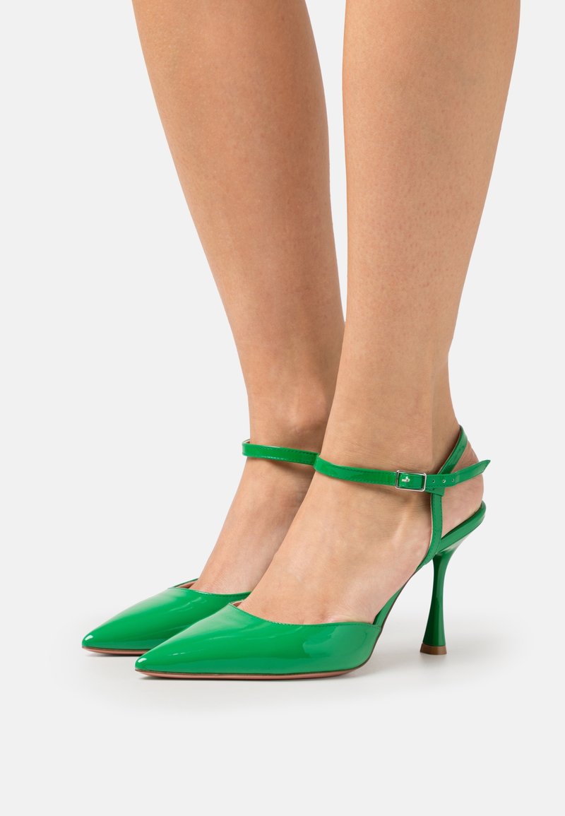 Zielone lakierowane szpilki z ostro zakończonym noskiem, paskiem w okolicy kostki i cienką szpilką. Gładkie, błyszczące wykończenie.
