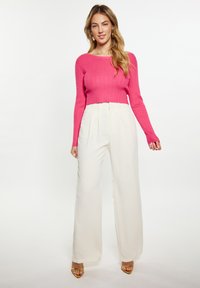 Rózsaszín, passzos, bordázott crop pulóver hosszú ujjakkal, fehér, széles szárú nadrággal párosítva. A modellen arany színű magassarkú szandál van.