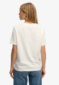 Cream-colored cotton t-shirt with short sleeves and a round neckline, featuring a plain back and a relaxed fit, paired with blue denim jeans.