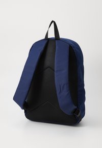 Marineblå ryggsekk med en teksturert svart maske bak, polstrede skulderstropper og et håndtak på toppen for bæring. Enkel og funksjonell design.