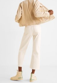 Beige corduroy jas, off-white cropped broek en beige high-top sneakers met groene accenten. Eenvoudig ontwerp met zichtbare stiksels.