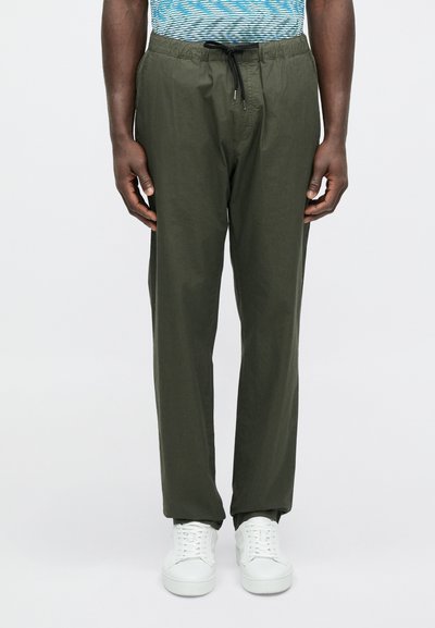 Ελαφριά παντελόνια με κορδόνι σε ελιά πράσινο χρώμα, με άνετη εφαρμογή και ελαστική μέση. Συνδυασμένα με λευκά αθλητικά παπούτσια, που αναδεικνύουν μια μίνιμαλ σχεδίαση.