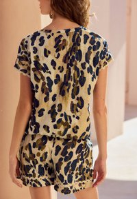 Komplet kratkih hlač in majice z kratkimi rokavi iz lahkega blaga s bež ozadjem, okrašen z modrim in zelenim leopardjim vzorcem.