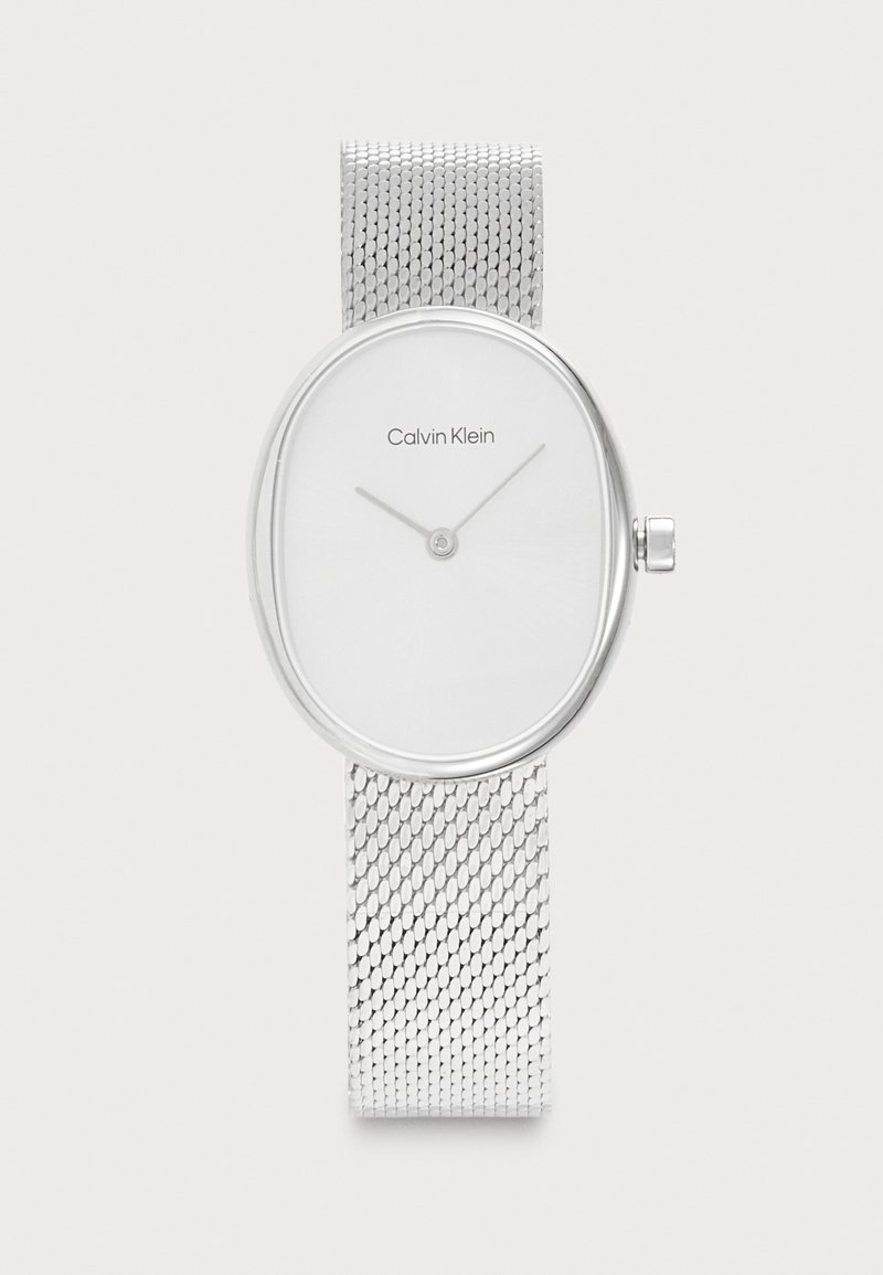Montre-bracelet Calvin Klein argentée avec cadran blanc ovale, aiguilles minimalistes pour les heures et les minutes, et bracelet en maille argentée.