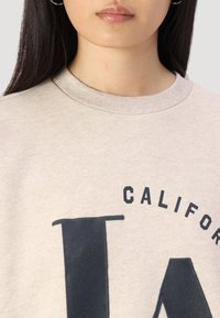 Felpa beige con collo a coste e grande scritta nera "CALIFORNIA LA" sul fronte. Materiale morbido con una finitura testurizzata.