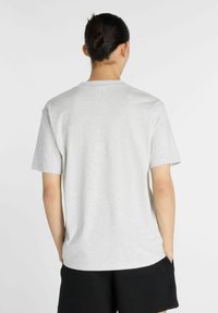 Camiseta de algodón gris con mangas cortas y cuello redondo, mostrada desde la parte de atrás. La tela parece suave con una textura sutil.