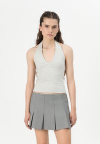 Svetlošedý halter top s hlbokým V-výstrihom, v kombinácii s sukňou s vysokým pásom a skladaným dizajnom, vyrobenou z hladkého materiálu.