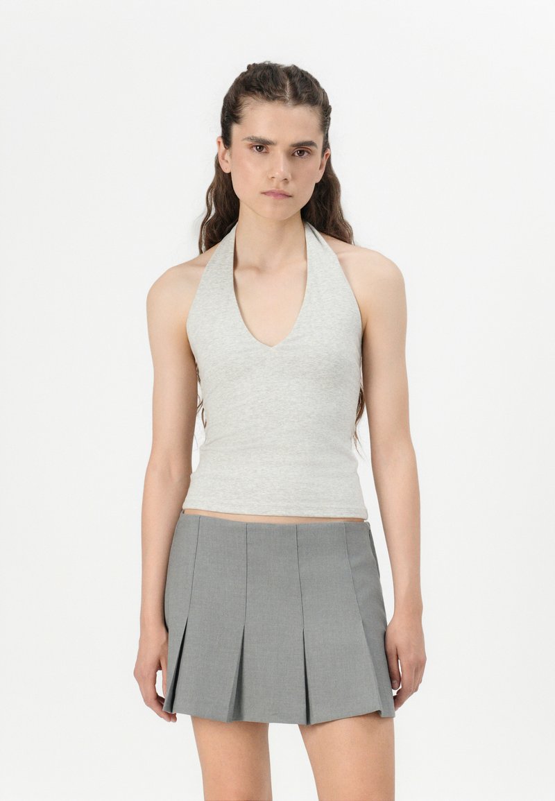 Svetlošedý halter top s hlbokým V-výstrihom, v kombinácii s sukňou s vysokým pásom a skladaným dizajnom, vyrobenou z hladkého materiálu.
