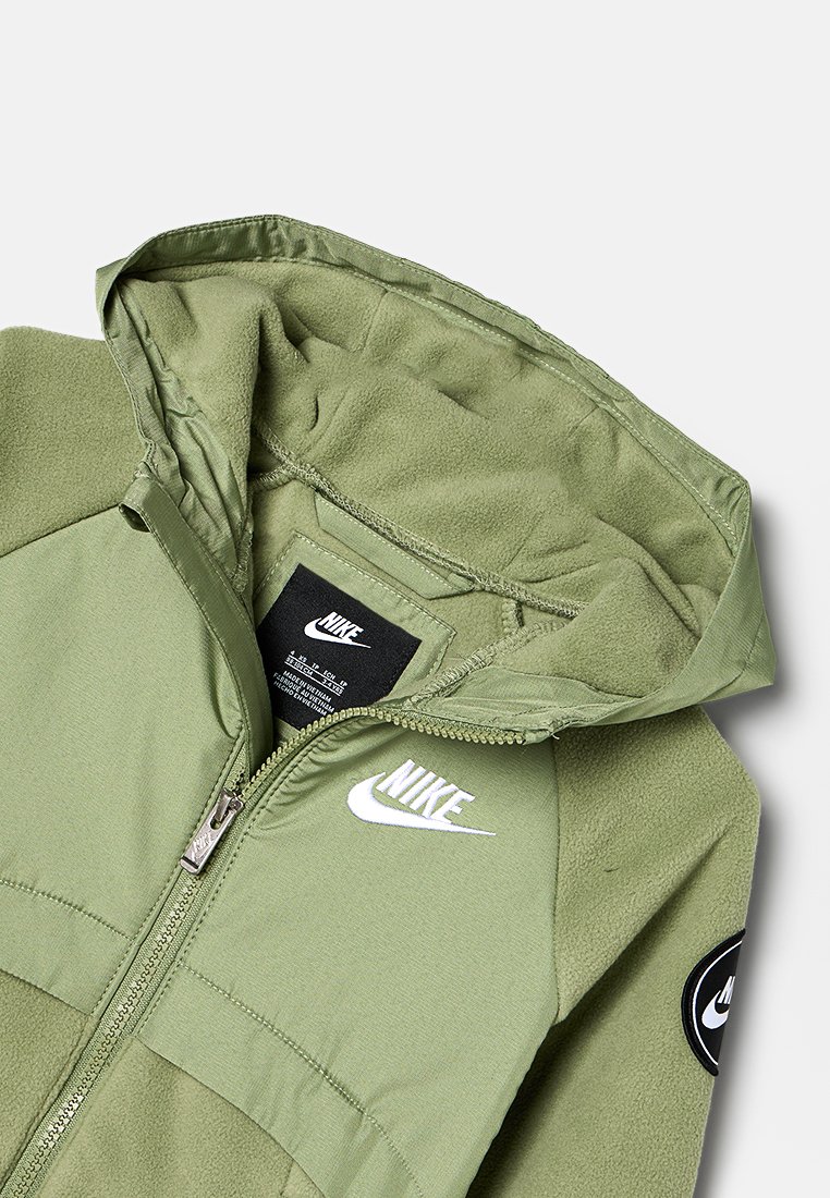 Veste Nike verte avec fermeture éclair, en matériau polaire, logo brodé et patch noir. Texture lisse avec une capuche et des accents contrastés.