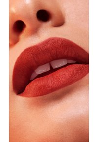 Matte, rötlich-brauer Lippenstift auf Nahaufnahme der glatten Lippen aufgetragen, weiße Zähne sichtbar und die natürliche Lippenform betonend.