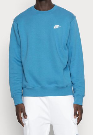 Sudadera azul de algodón con mangas largas, puños y dobladillo de canalé, que presenta un logo blanco de Nike en el lado izquierdo del pecho. Textura suave.