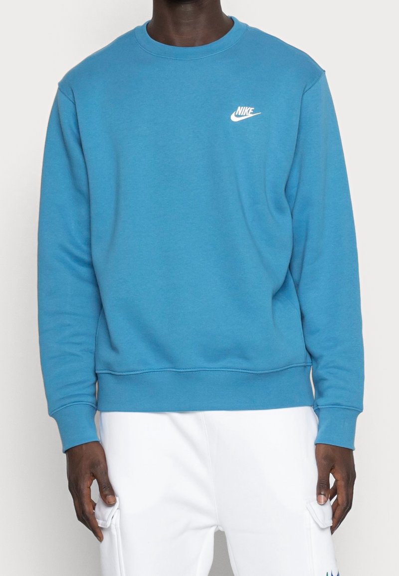 Sudadera azul de algodón con mangas largas, puños y dobladillo de canalé, que presenta un logo blanco de Nike en el lado izquierdo del pecho. Textura suave.