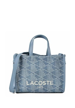 Sac à main en jean bleu Lacoste avec motif géométrique, deux poignées, une bandoulière et "LACOSTE 1933" imprimé à l'avant.