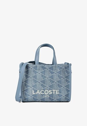 Sac à main en jean bleu Lacoste avec motif géométrique, deux poignées, une bandoulière et "LACOSTE 1933" imprimé à l'avant.