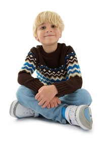 Brun stickad tröja med blåa, krämfärgade och svarta zigzag-mönster, kombinerad med ljusa jeans och vita sneakers med blå detaljer.