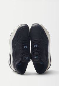 Sneaker nere con una suola bianca spessa, caratterizzate da una tomaia testurizzata, lacci e branding con accenti blu, e un design a punta arrotondata.