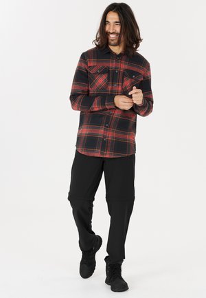 Flanellen overhemd in rood en zwart plaid, met twee borstzakken; gecombineerd met zwarte ritsbroeken en zwart schoeisel.