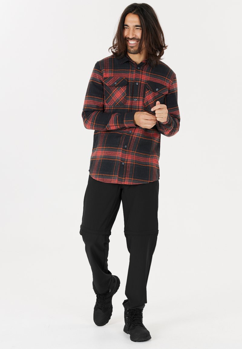Rutigt flanellskjorta i röd och svart, med två bröstfickor; kombinerad med svarta byxor med dragkedja och svarta skor.